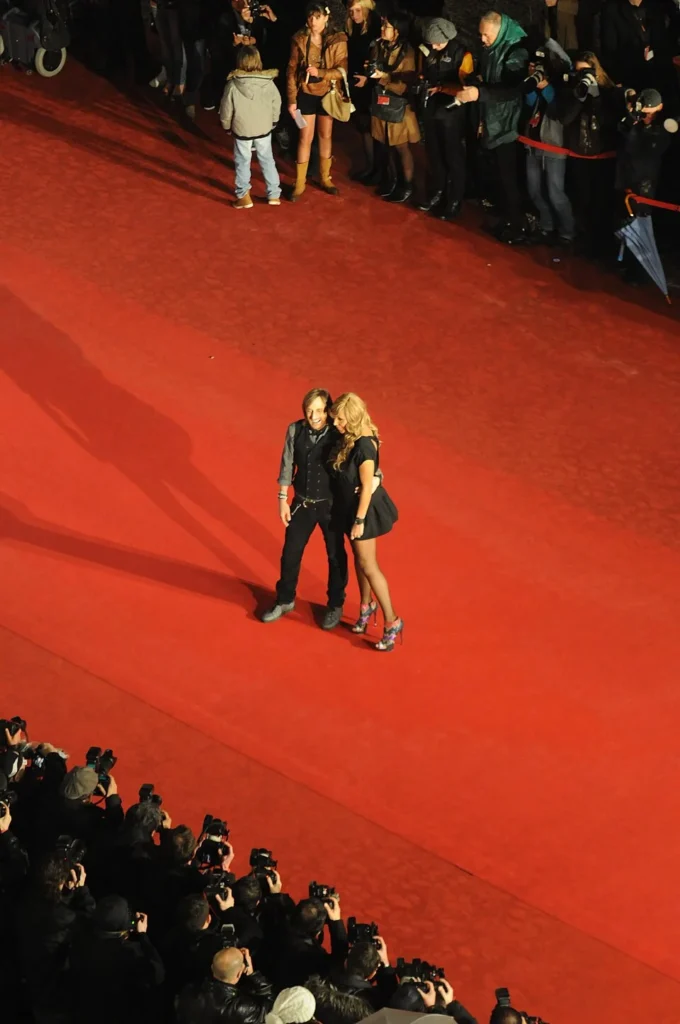 David Guetta and partner walking on a red carpet surrounded by photographers